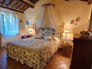 Um quarto com uma cama, uma mesa de cabeceira, uma luminária, uma janela com cortinas e um relógio de parede.