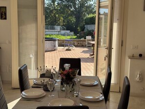 A dining area with a table set for four, a vase with flowers, and a view of the outdoor patio. - Villa al Glicine Proprietà by Interhome (Altopascio)