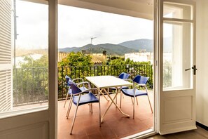 An open balcony with a table and chairs, a view of mountains, and a building in the background. - 110 Port de la Selva - House close to the beach (Port De La Selva, El)