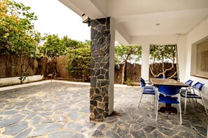 An outdoor patio with stone flooring, a stone pillar, a table with chairs, and a view of trees and a fence. - 110 Port de la Selva - House close to the beach (Port De La Selva, El)