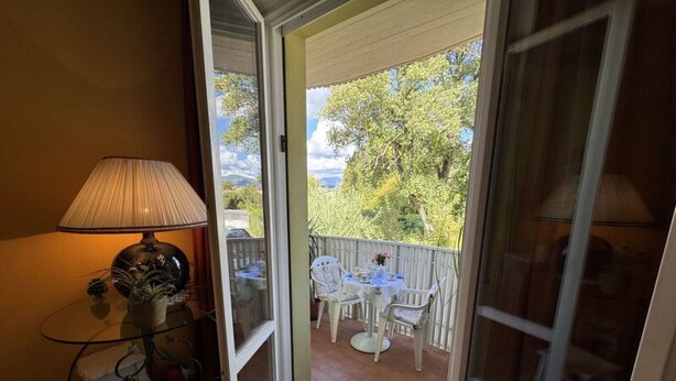 Quarto com porta de vidro deslizante que dá para um pátio externo com mesa e cadeiras.