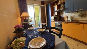 Uma área de refeições com uma mesa posta para dois, uma cozinha com armários azuis e vista para o exterior.