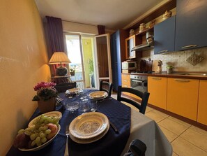 Ein Essbereich mit einem Tisch für zwei Personen, eine Küche mit blauen Schränken und Blick ins Freie.