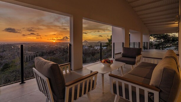 Un espace extérieur moderne aménagé avec des sièges, offrant une vue sur le coucher de soleil au-dessus d’une ville.