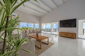 Ein geräumiges Wohnzimmer mit großem Fenster, einem Holztisch, einer Couch und einem an der Wand befestigten Fernseher.