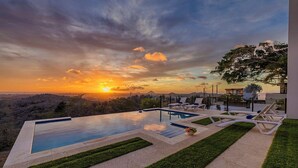 Une piscine avec des chaises longues, une vue sur le coucher de soleil et un jardin aménagé.