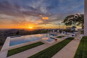 Una piscina con sillas de descanso, vistas al atardecer y un jardín ajardinado.
