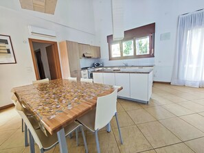 A modern kitchen with white cabinets, a dining table with chairs, and a window with curtains. - Ferienvilla Beethoven by Interhome (Lignano Pineta)