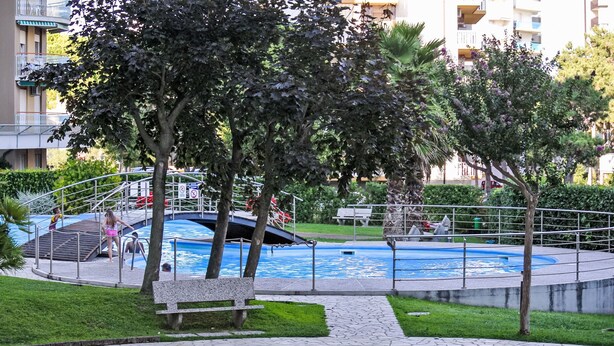 Un área de piscina con una fuente circular de agua, rodeada de árboles y un banco.
