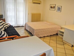 A room with a bed, a table, a chair, a radiator, and a window with curtains. - Villa Maria 2 by Interhome (Lignano Pineta)