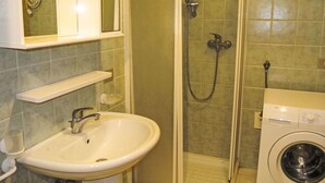 Een badkamer met een wastafel, spiegel, douche en wasmachine.