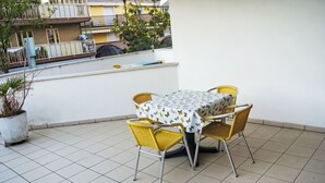Een terras met een tafel en stoelen, een plant in pot en gebouwen op de achtergrond.