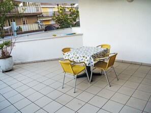 A patio with a table and chairs, a potted plant, and a view of buildings in the background. - Villa Maria 2 by Interhome (Lignano Pineta)