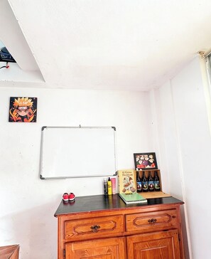 Una pizarra, un mueble de madera con cajones, un cuadro enmarco y una estantería pequeña con botellas y un libro.