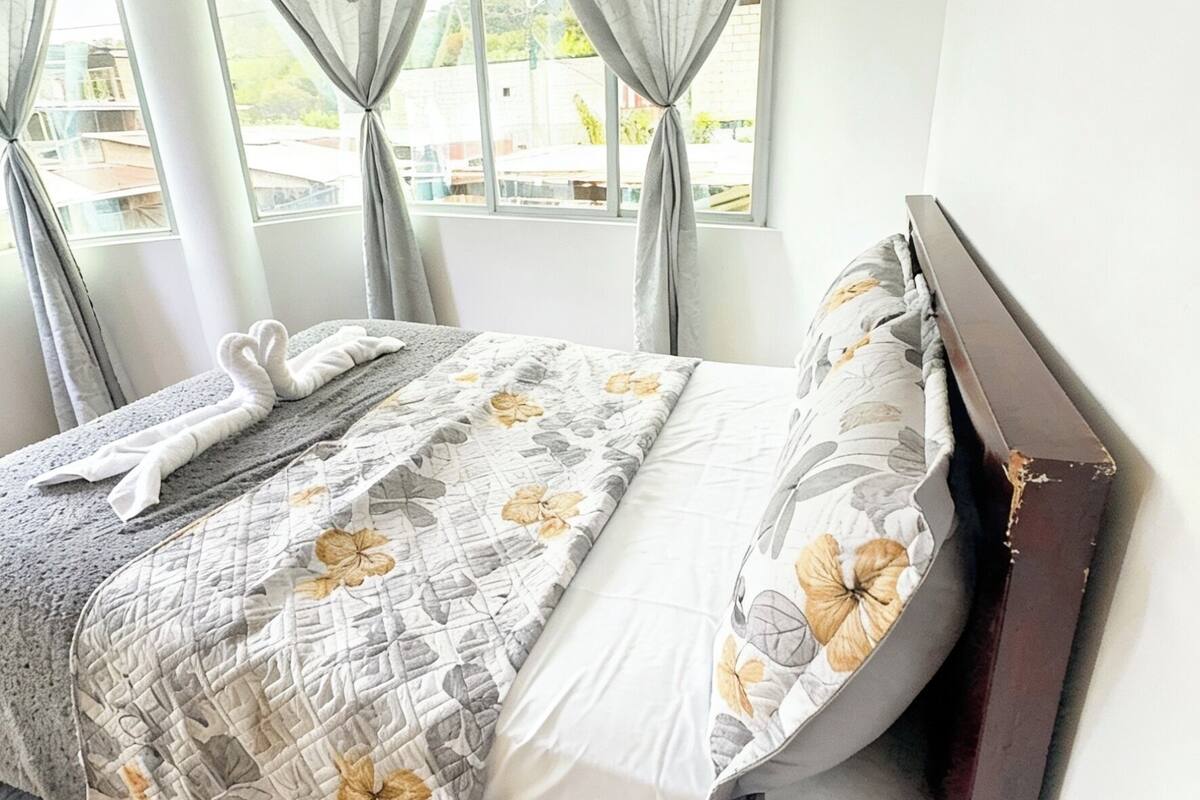 A neatly made bed with a floral bedspread, a wooden headboard, and curtains on a window.