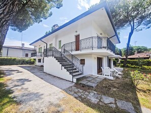 Ein zweistöckiges Haus mit Balkon, Treppe und einer Terrasse mit Gartenmöbeln.