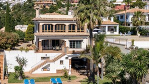 Et stort hus med swimmingpool, udendørs møbler og en trappe til en balkon.