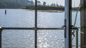 A view from a boat's deck with a metal railing, a bench, and a glass door leading to the water.