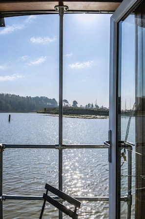 Une vue prise depuis le pont d’un bateau, avec une rambarde en métal, un banc et une porte vitrée donnant sur l’eau.