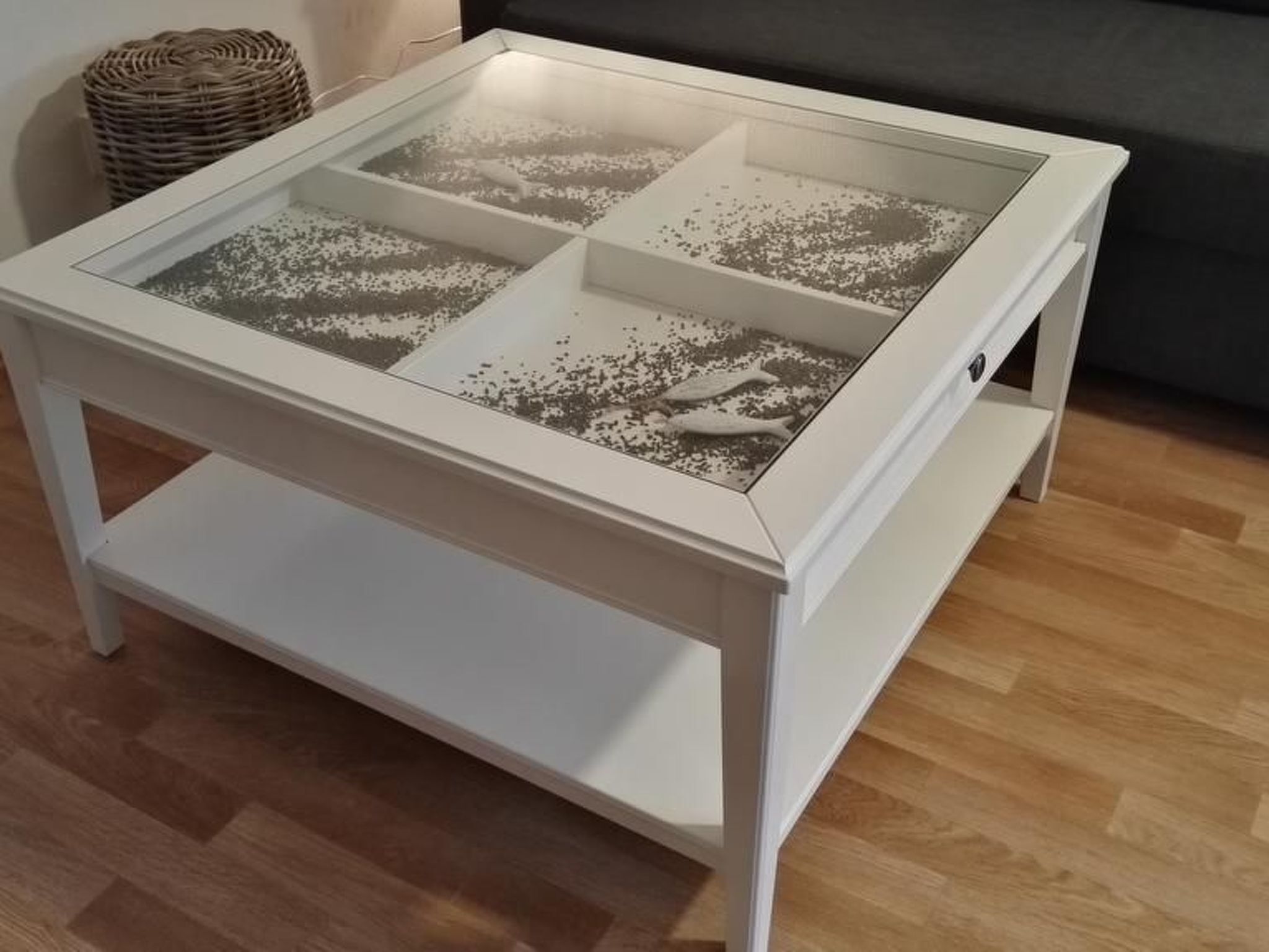 Ett vitt bord med glasskiva och en hylla under, placerat på ett trägolv.