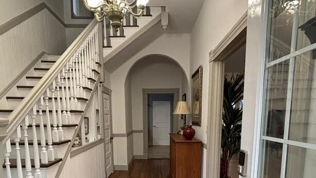 Un couloir doté d’un plancher en bois, d’un lustre, d’un escalier et d’une porte à panneaux de verre.