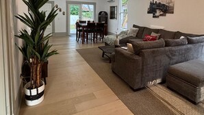 A spacious living room with a grey sectional sofa, a dining area with a table and chairs, and a large potted plant. - Charming Remodeled 1920 Country Home Retreat 3 Bed 2 Bath (Waycross)