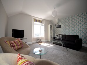 A living room with a sofa, a glass coffee table, a TV, a bookshelf, and patterned wallpaper. - in Torquay by Interhome (Torquay)