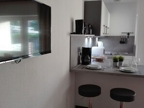 Eine moderne Küche mit Flachbildfernseher, Kaffeemaschine, Mikrowelle und zwei Barhocker.