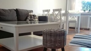 Ein modernes Wohnzimmer mit einem weißen Esstisch, einem grauen Sofa und einem Korbstuhl.