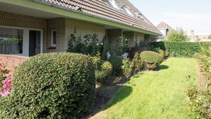 Ein zweistöckiges Haus mit Ziegeldach, Backsteinfassade und einem gepflegten Garten mit Hecken und Rasen.