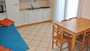 Cocina pequeña con armarios blancos, cocina a gas y lavamanos. Hay una mesa de comedor con sillas y un sofá azul con un cojín naranja.
