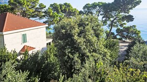A building with a red-tiled roof, surrounded by dense greenery and overlooking a body of water. - Kiefer Vordach Duplex Studio A4 by Interhome (Brela)