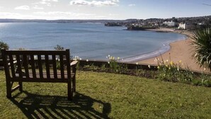 A bench overlooking a beach with a view of the sea and distant buildings. - Modern eingerichtete Ferienwohnung in der ersten Etage mit Panorama-Meerblick v by Interhome (Torquay)