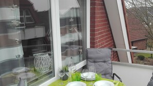 A dining area with a table set for two, a window with a view of a brick building, and a chair with a cushion. - Wat(t) ne Wohnung by Interhome (Büsum)