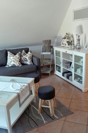 Ein Wohnzimmer mit einer Couch, einem kleinen Tisch, einem Schrank und einem Hocker.
