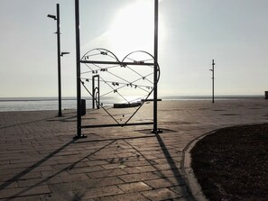 Eine herzförmige Skulptur am gepflasterten Weg entlang des Strandes.