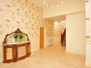 Ein Flur mit gemustertem Wandpapier, einem Holzkonsolentisch und einer Treppe.