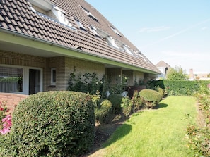 Ein zweistöckiges Haus mit Ziegeldach, Backsteinfassade und einem gepflegten Garten mit Hecken und Rasen.
