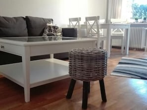 Ein modernes Wohnzimmer mit einem weißen Esstisch, einem grauen Sofa und einem Korbstuhl.