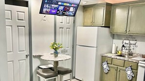 A modern kitchen with a flat-screen TV mounted above a dining table, a refrigerator, and green cabinets.