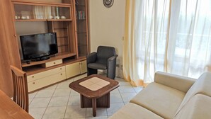 A living room with a television on a wooden stand, a grey armchair, a beige sofa, and a small wooden coffee table. - Billa 2 in grüner Lage by Interhome (Lignano Sabbiadoro)