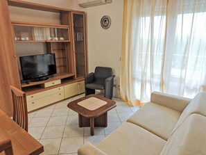 A living room with a television on a wooden stand, a grey armchair, a beige sofa, and a small wooden coffee table. - Billa 2 in grüner Lage by Interhome (Lignano Sabbiadoro)