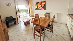 A dining area with a wooden table and chairs, a sofa, and a view through a glass door to an outdoor space. - Billa 2 in grüner Lage by Interhome (Lignano Sabbiadoro)