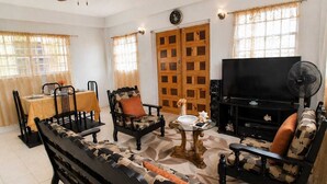 Un salon comprenant un canapé, des fauteuils, un téléviseur, un ventilateur et un coin repas avec une table et des chaises.
