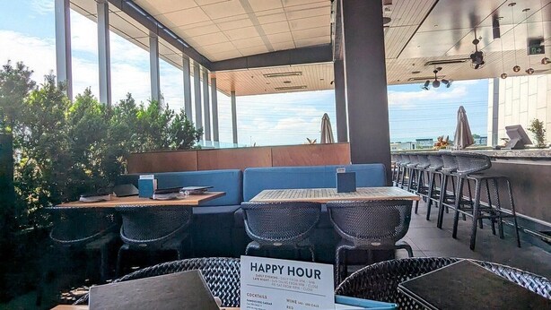 An outdoor seating area with tables and chairs, a 'HAPPY HOUR' sign, and a view of the sky. - Lib3rtie Suites -2BR Family Suite •Sleeps 6 •Full Kitchen •Laundry •Free Parking (Saskatoon)
