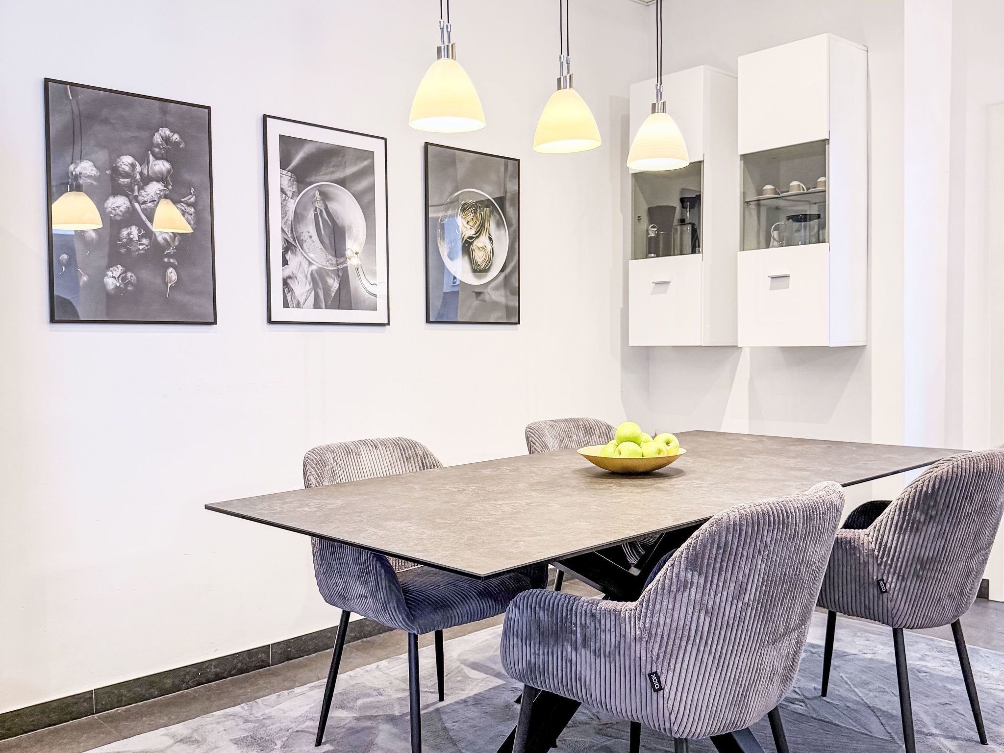 Ein moderner Essbereich mit einem rechteckigen Tisch, sechs gepolsterten Stühlen und drei gerahmten Kunstwerken an der Wand.