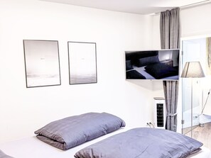 A modern hotel room with a bed, two pillows, a flat-screen TV, and a window with curtains.