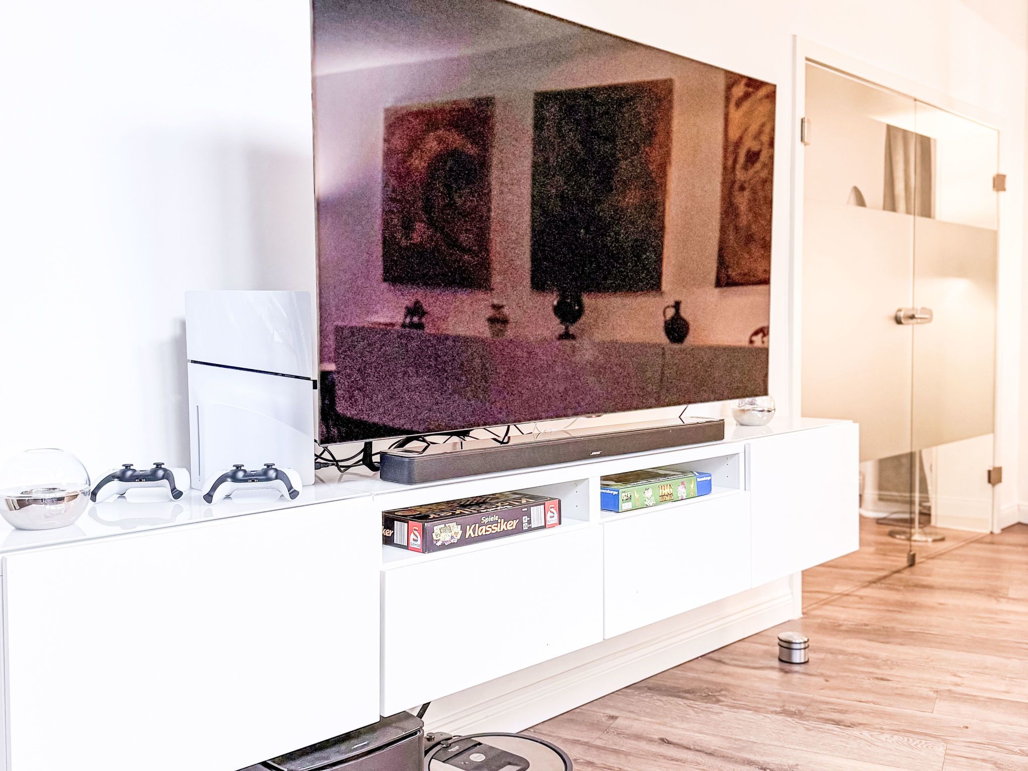 Ein modernes Wohnzimmer mit einem flachbildfernseher an einer weißen Unterhaltungsanlage, einer Spielkonsole und einigen Brettspielen.