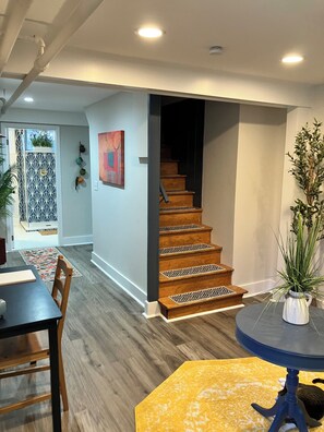 Eine Treppe mit Holzbeschlägen und gemusterten Tritten, ein Essbereich mit Tisch und Stühlen sowie ein Blumentopf auf einem Tisch.