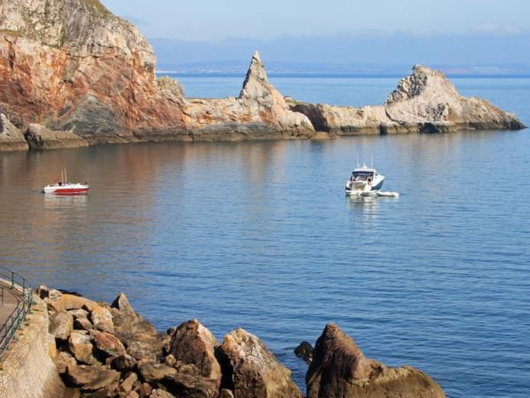 A coastal scene with rocky cliffs, calm water, and boats.